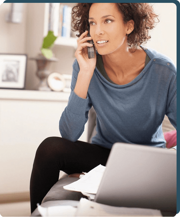 Woman talking on phone near laptop, smiling.